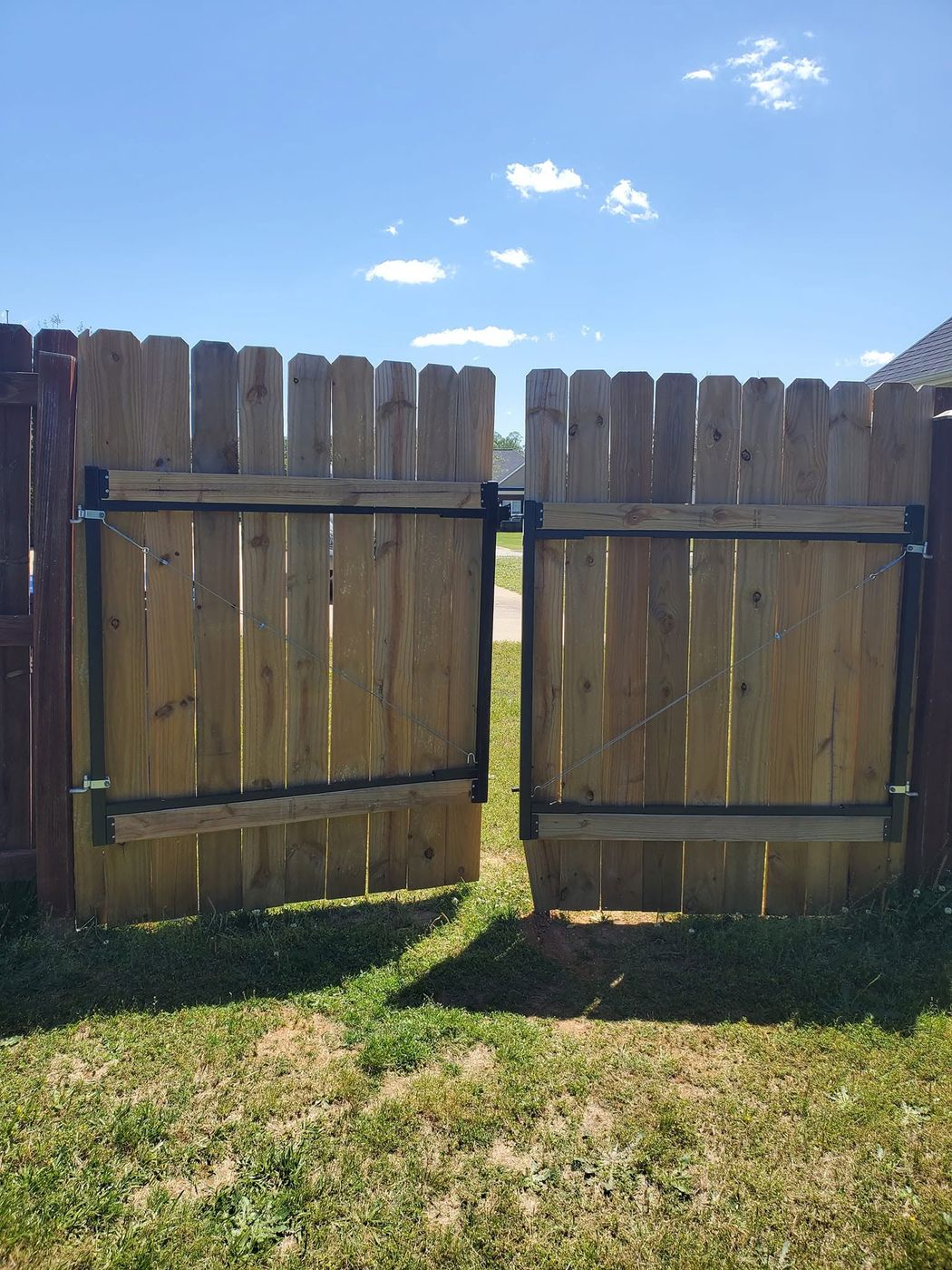 Two wood gates on black steel frames in a privacy fence